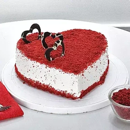 Anniversary Red Velvet Cake (MB408) from the best bakery cakes shop in Aligarh, heart-shaped red velvet cake with creamy white frosting, rich red crumb topping, and elegant chocolate décor